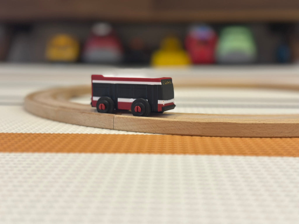 Small toy train on a wooden track with colorful blurred objects in the background