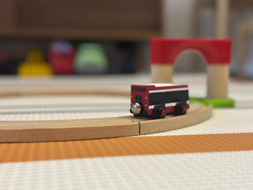 Small red toy truck on a wooden track with a blurred background